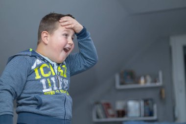 the boy is standing,holding his head with one hand and looking at the TV screen in surprise because he finally successfully completed a difficult mission in a video game.emotional moment of a gamer