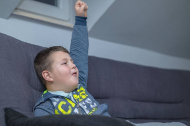 a boy is playing a video game. the boy raised his hand and celebrates the success he achieved in the video game. Mission successfully completed
