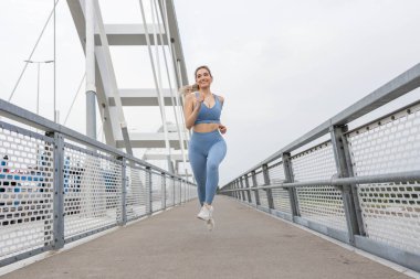 Köprüde koşan güzel, sportif genç bir kadın. Güçlü vücut ve bacaklara sahip kadın koşucu köprüden ve eğitimden geçiyor. Spor ve eğlence..