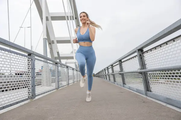 Köprüde koşan güzel, sportif genç bir kadın. Güçlü vücut ve bacaklara sahip kadın koşucu köprüden ve eğitimden geçiyor. Spor ve eğlence..