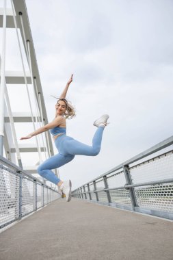 Genç sporcu köprüde neşeyle zıplıyor. Spor giyim kuşamı giyiyor. Eğitimini yeni bitirdi ve çok mutlu. Özgürlük kavramı.