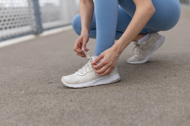 Ayakkabı bağcıklarını yolda bağlayan genç atletik kadın.