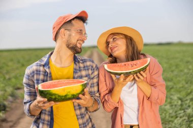 Tarlada genç ve güzel bir çiftin portresi. Ellerinde olgun bir karpuzun iki yarısı ve gülümsüyor.