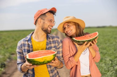 Tarlada genç ve güzel bir çiftin portresi. Ellerinde olgun bir karpuzun iki yarısı ve gülümsüyor.