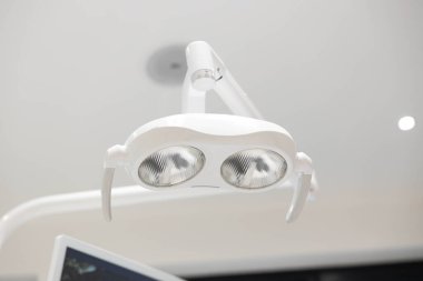 A modern dental lamp with dual circular lights, mounted in a pristine dental clinic, showcasing the advanced equipment used for dental procedures. clipart