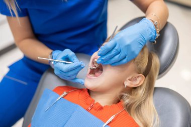 Eldivenli bir dişçi, diş aletlerini kullanarak çocuğun dişlerini inceler, kapsamlı bir sağlık kontrolü sağlar ve modern bir klinikte diş bakımı sağlar..