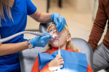 Modern diş sağlığı uygulamalarının hassasiyetini ve önemini gösteren, profesyonel bir dişçiden diş tedavisi gören küçük bir çocuğun yakın çekimi.