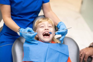 Happy child at the dentist showing a big smile, examined by a dental hygienist, illustrating a positive dental experience in a professional setting. clipart