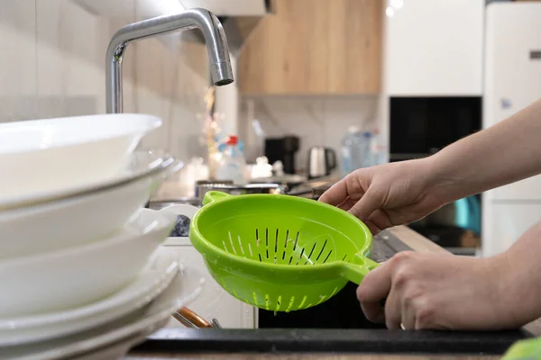 Close-up of a sink in the kitchen with dishes, a bright colander in female hands