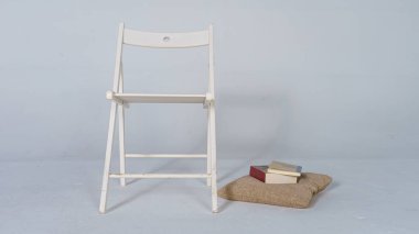 Çalışma odasındaki yastığın yanında minimalist, beyaz, tahta bir sandalye. Yastığın üstünde iki kapalı kitap var. İç tasarım kavramı