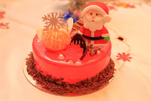 Red cake decorated with a Santa figure and a natural orange, blurred image in the back