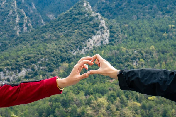 Two hands touching each other making the shape of the heart with a mountainous and cloudy background where only the hands are illuminated
