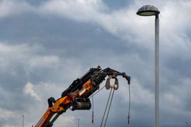 Arka planda bulutlu gökyüzü ve yanında lamba direği olan turuncu turuncu vinç..