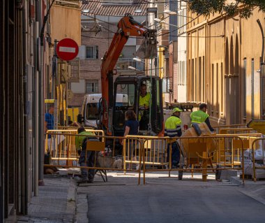 Granollers 'da bir sokakta kamu işlerinde çalışan işçiler. Koruma çitleri ve kepçeler. Beton karıştırıcı.