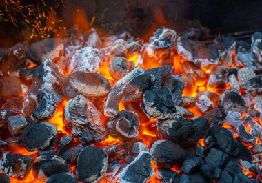 Metal bir barbeküde kömür ve közler tam kapasite yanıyor.