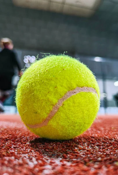 Detail shot of a paddle ball on the floor of the indoor paddle tennis court and three player friends in the background of the court
