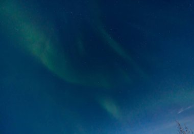 Green and purple northern lights in iceland with the sky bluish by the moon