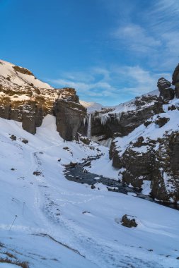 Group of mountaineering tourists on a route through a totally snowy road between the mountains towards the Seljalandsfoss waterfall with the dawn sun illuminating the snowy mountain tops of Iceland