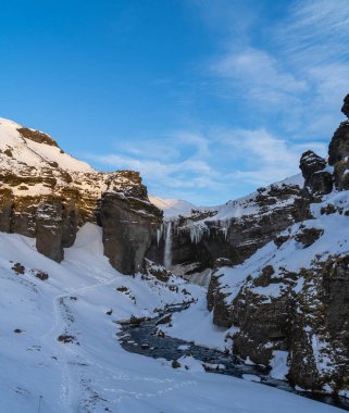 Group of mountaineering tourists on a route through a totally snowy road between the mountains towards the Seljalandsfoss waterfall with the dawn sun illuminating the snowy mountain tops of Iceland