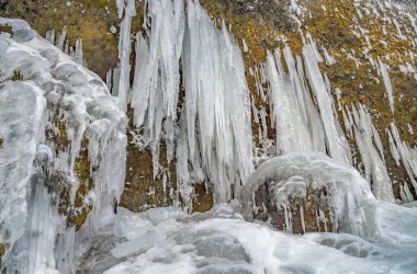 Icy stalagmites created from the side of a mountain next to the Kvernufoss waterfall, surrounded and covered with snow as if it were an ice curtain or ice fangs.