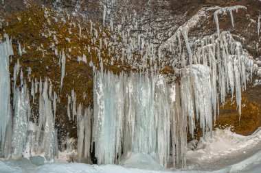Icy stalagmites created from the side of a mountain next to the Kvernufoss waterfall, surrounded and covered with snow as if it were an ice curtain or ice fangs.