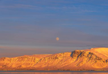 Dolunayın görüldüğü Reykjavik şehri kıyılarında gün batımı ve akşam güneşiyle aydınlanan Engey ve Videy adaları.