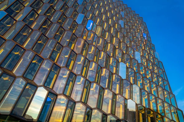 stock image Detail of the avant-garde architecture structure and facade of the windows and glass doors of the Harpa concert building and conference center illuminated by the morning sun, reflecting its light and colors and simulating a beehive. It is home to the