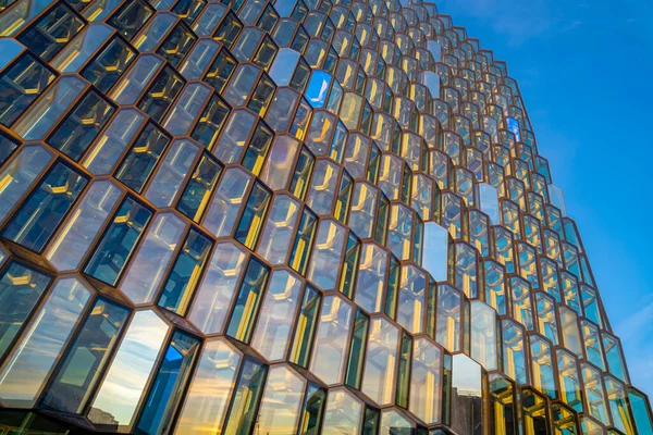 stock image Detail of the avant-garde architecture structure and facade of the windows and glass doors of the Harpa concert building and conference center illuminated by the morning sun, reflecting its light and colors and simulating a beehive. It is home to the