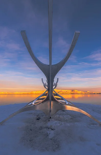 Conceptual metallic sculpture of the Viking boat from The Sun Voyager of the city of Reykjavik from behind and with a symmetrical perspective, where the full moon and the islands of Engey and Videy are seen illuminated by the twilight or sunset sun