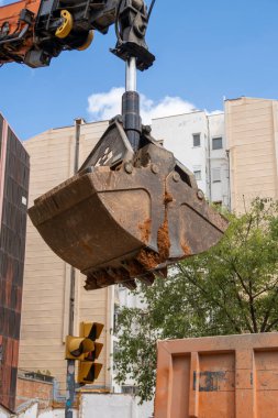 Hidrolik kova kazıcı küreği inşaat güvenlikli ilan panosu olan şehir sokağındaki kazı ve restorasyon çalışmalarında kamyona toprak yükleyip bırakıyor.