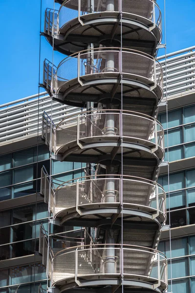 stock image Circular iron staircase for fire escape outside a modern metal industrial building fence in the open air.
