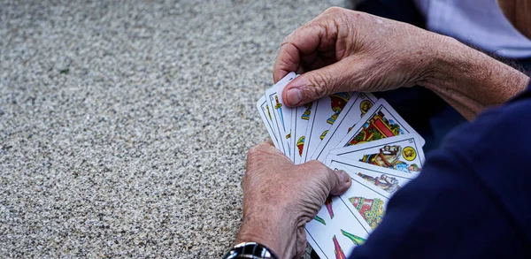 Senior and retired person playing with a deck of Spanish cards on a granite stone table in a rural mountain village