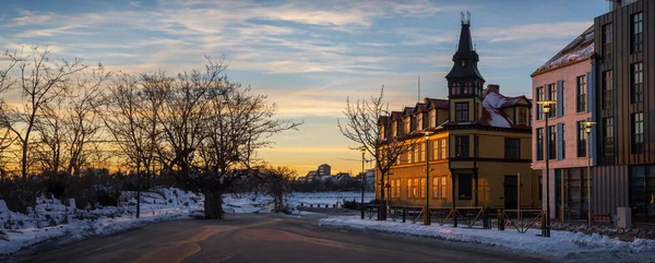 Stock image Facade of typical Reykjavik houses illuminated by the last rays of the evening sun reflecting orange and gold light with snowy sidewalks and a subtly cloudy sky with twilight tones