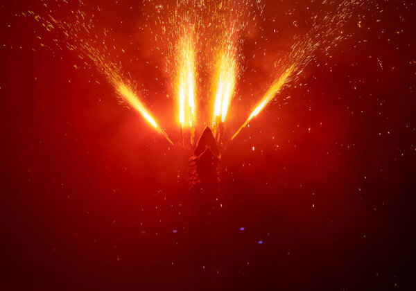 Голова дракона смотрит вверх, изгоняя фейерверки из своих крыльев и создавая ливень из огненных искр, которые падают и тускло освещают тьму подземного мира или ад в красном