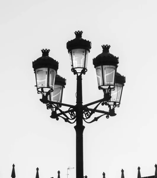 Silhouette of a wrought iron street lamp with five lanterns hand-decorated with opaque glass and a silhouette of a TV antenna and the peaks of the palace of the palace in the Plaza Mayor of Salamanca
