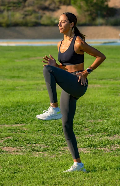 Beautiful young slim, tanned runner with long hair tied in a ponytail, concentrated with her eyes closed practicing technical running movements, flexing and lifting her legs.