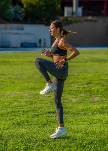 Beautiful young slim, tanned runner with long hair tied in a ponytail, concentrated practicing technical running movements, flexing and lifting her legs.
