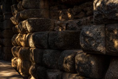 Merida 'daki antik Roma Tiyatrosu' nun merdivenlerini çevreleyen duvardan taş ve taş bloklar. Arka plandaki kemerli kapı, dalın gölgeleri arasındaki güneş ışığıyla aydınlanıyor.