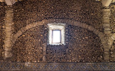 Duvar, istiflenmiş insan kafatasları ve kemiklerle yaratılmış bir kemerle süslenmiş. Şapel. Evora. Portekiz. Üç Fransisken rahibin girişimiyle yaratıldı..
