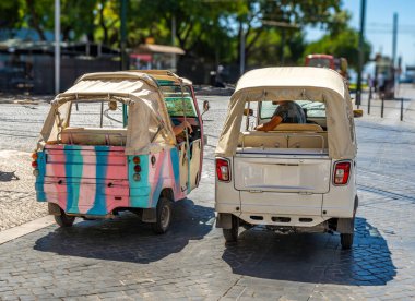 İki Piaggio Ape Calessino 200 üç tekerlekli turist Tuk Tuk, Lizbon 'da bir kaldırım taşı caddesine park etmiş, yerde tramvay rayları var..