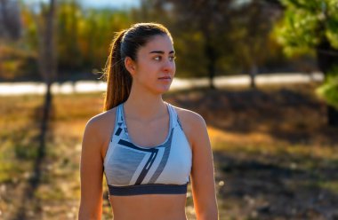 At kuyruklu güzel bir kız, spor bir bluz giyiyor, sakin ve huzurlu görünüyor ve gülümsüyor. Şafak güneşiyle aydınlanıyor. Muhteşem bir orman ve yeşil bir yaprak..