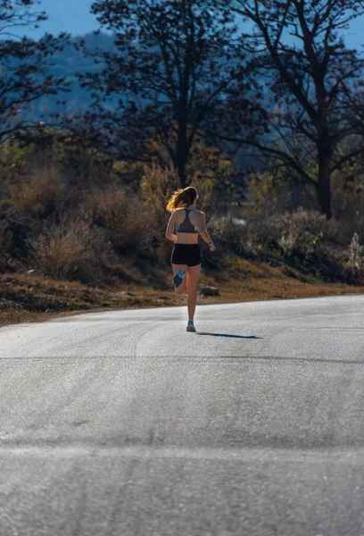 Şafak sökerken arka planda kalan genç bir koşucu kız bir doğa parkında asfalt üzerine gölgesini düşürerek havada asfalt bir şekilde asılı duruyor..