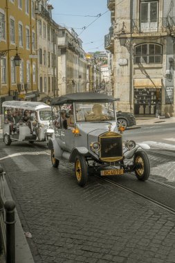 Turistler ve aileler, eski elektrikli bir turist arabasının ve üç tekerlekli bir aracın parke bir Lizbon caddesindeki tepeye tırmanışının fotokopisini çekiyorlar..