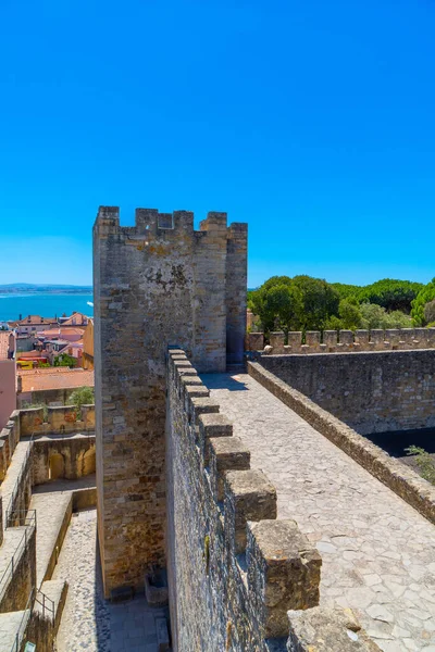 Top view of the walls, barbican, wall and walkway to the watchtower or tribute of the Castle of Saint George with part of the typical houses of Lisbon, and the Tagus River in the background.