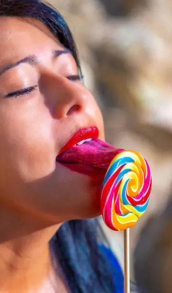 Young brunette Latina with bright red sensual lips passionately licking a colorful spiral lollipop with the tip of her beautiful sensual long pink tongue sticking out with her mouth open.