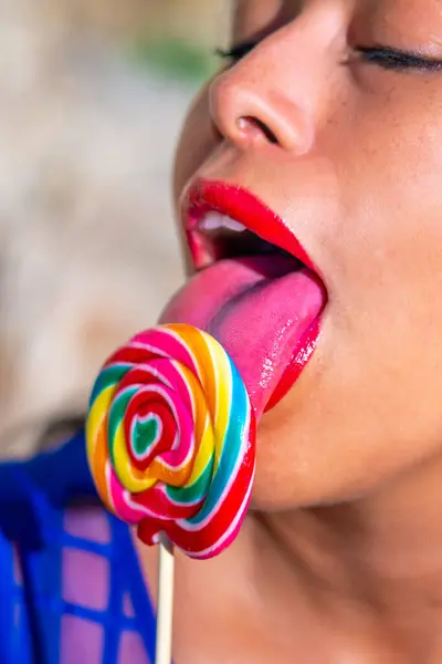 Young sexy Latina with bright red sensual lips passionately licking a colorful spiral lollipop with her beautiful sensual long pink tongue sticking out with her mouth open.
