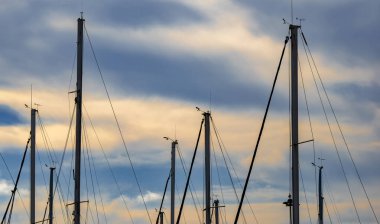 Yat direkleri ve yelkenlilerin arka ışıklandırılmış siluetleri gökyüzünün altındaki bir limana yanaşmış akşam güneşiyle bulutları aydınlatıyordu. Büyülü ve romantik gökyüzü.