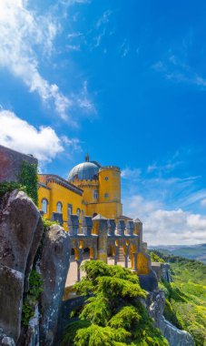 Pena Sarayı 'nın kemerli avlusunun dış görünüşü, sarıya boyanmış, büyük kayalara tünemiş, fotokopi alanı için güneşli mavi gökyüzünün altında Sintra sıradağları var..