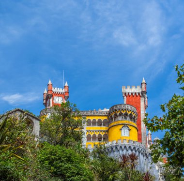 Pena Sarayı 'nın altından yeşillik ve masmavi bir gökyüzünün altında palmiye ağaçlarıyla kaplı duvarlar üzerinde sarı ve kırmızı renkte bir manzara. Sintra. Portekiz.