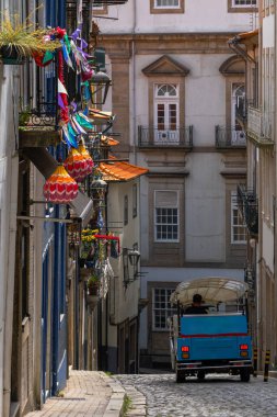 Mavi tuktuk, renkli kağıt bayraklar, fenerler, çiçekler ve saksılarla süslenmiş Porto 'nun eski, klasik bir mahallesindeki eski evlerin balkonlarıyla yokuş aşağı bir kaldırım taşından aşağı iniyor. Portekiz.